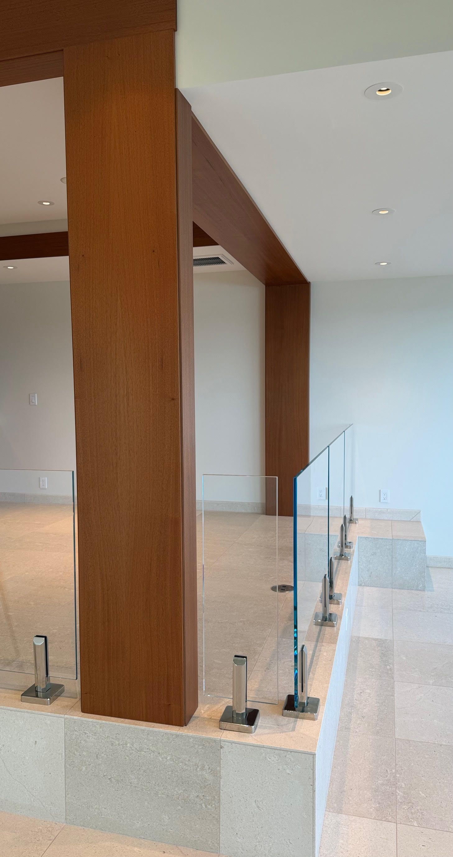 Modern kitchen with a large wooden pillar, glass railing, and beige stone counters in a bright open interior