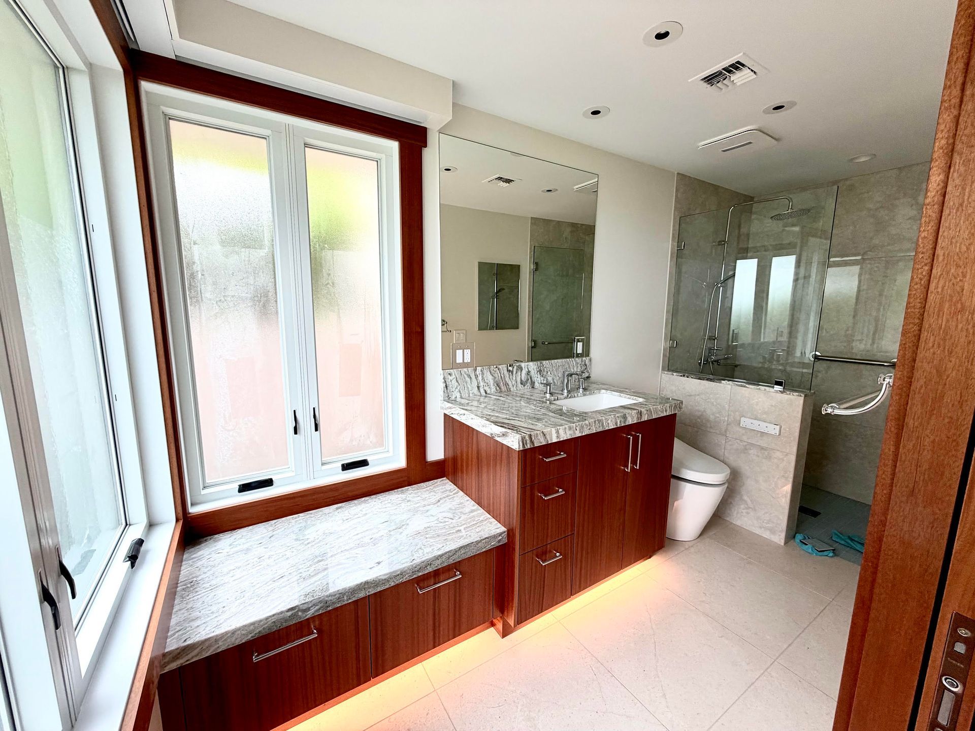 Bright bathroom with vanity, large window, mirror, and glass shower enclosure