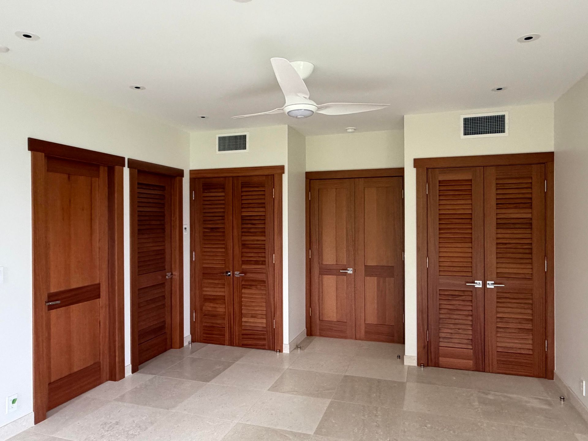 Empty beige room with multiple wooden closet doors, tiled floor, and a ceiling fan