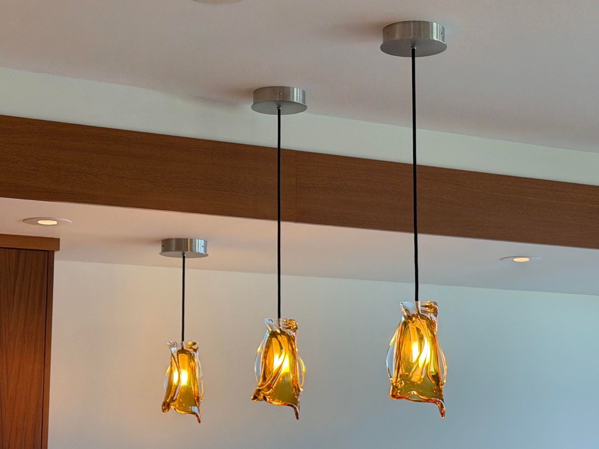 Three amber pendant lights hanging from a wooden beam on a white ceiling.