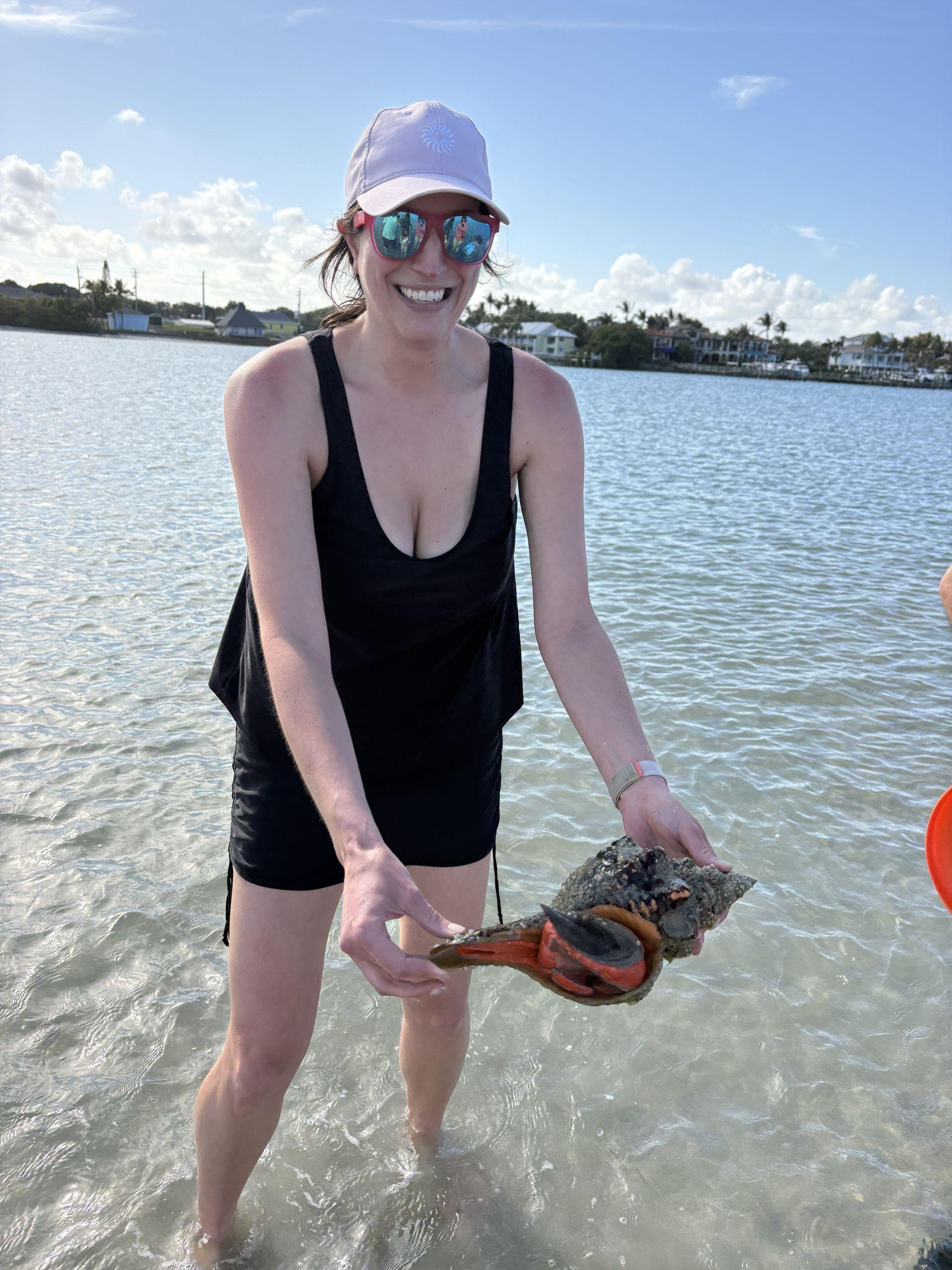 Person in black swimsuit holding a crab while standing in shallow water by the shore.