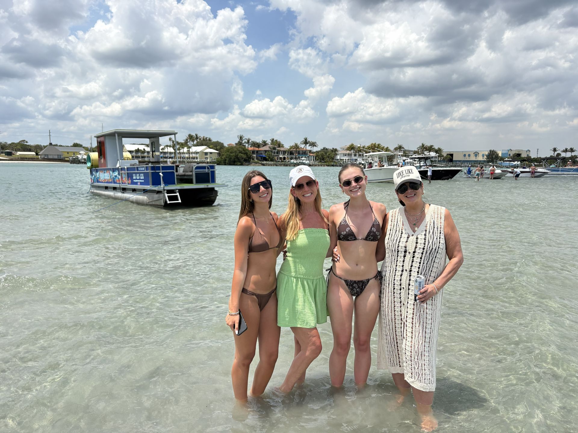 Four people posing in shallow water beside a blue boat under a cloudy sky