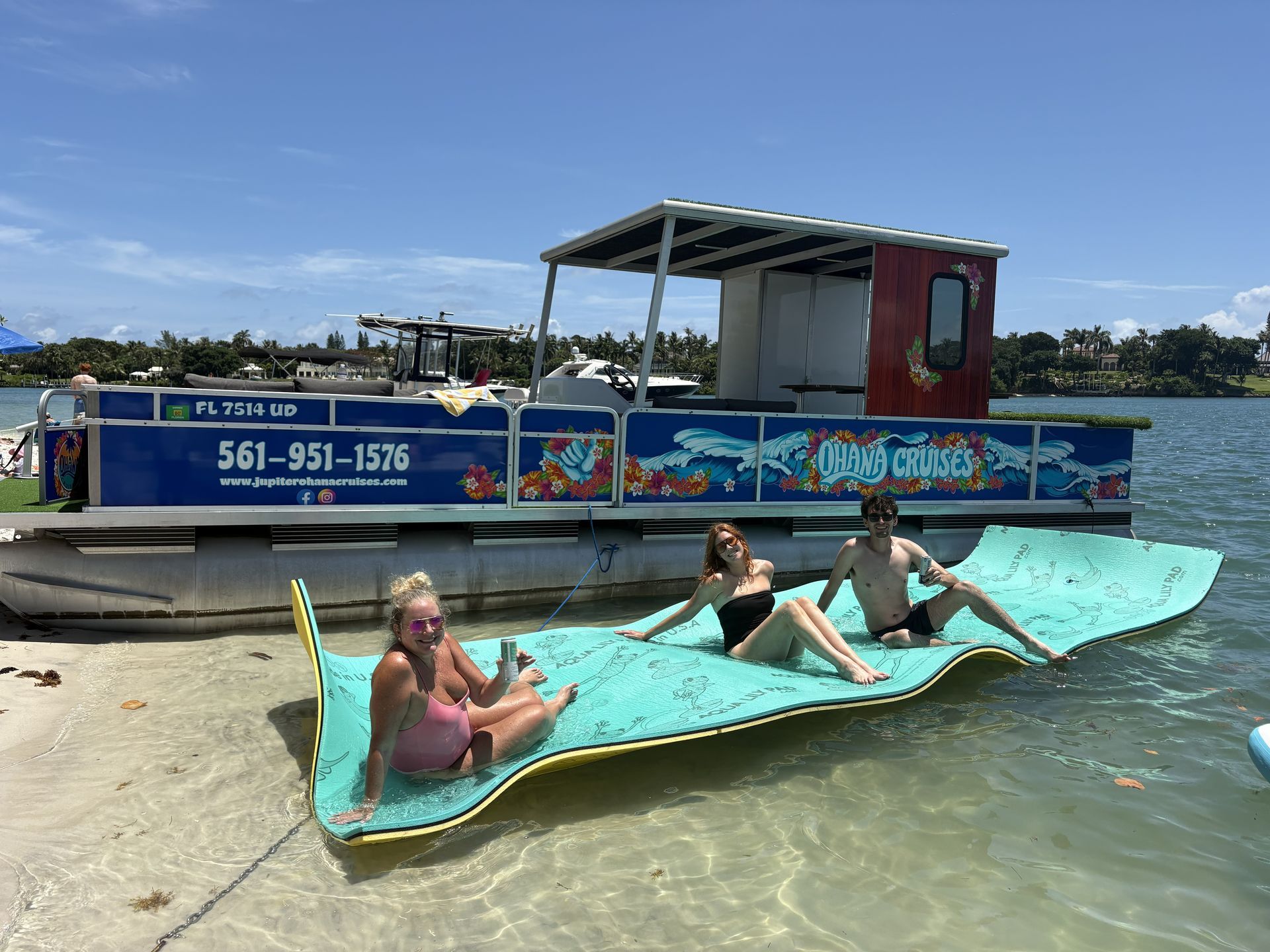 People relaxing on a turquoise paddleboard beside a colorful boat on calm water.