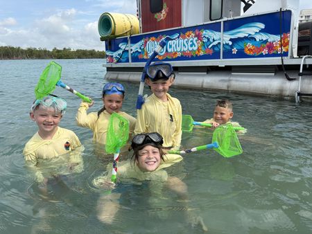 Five people in yellow shirts and snorkel gear play in shallow water beside a colorful boat.