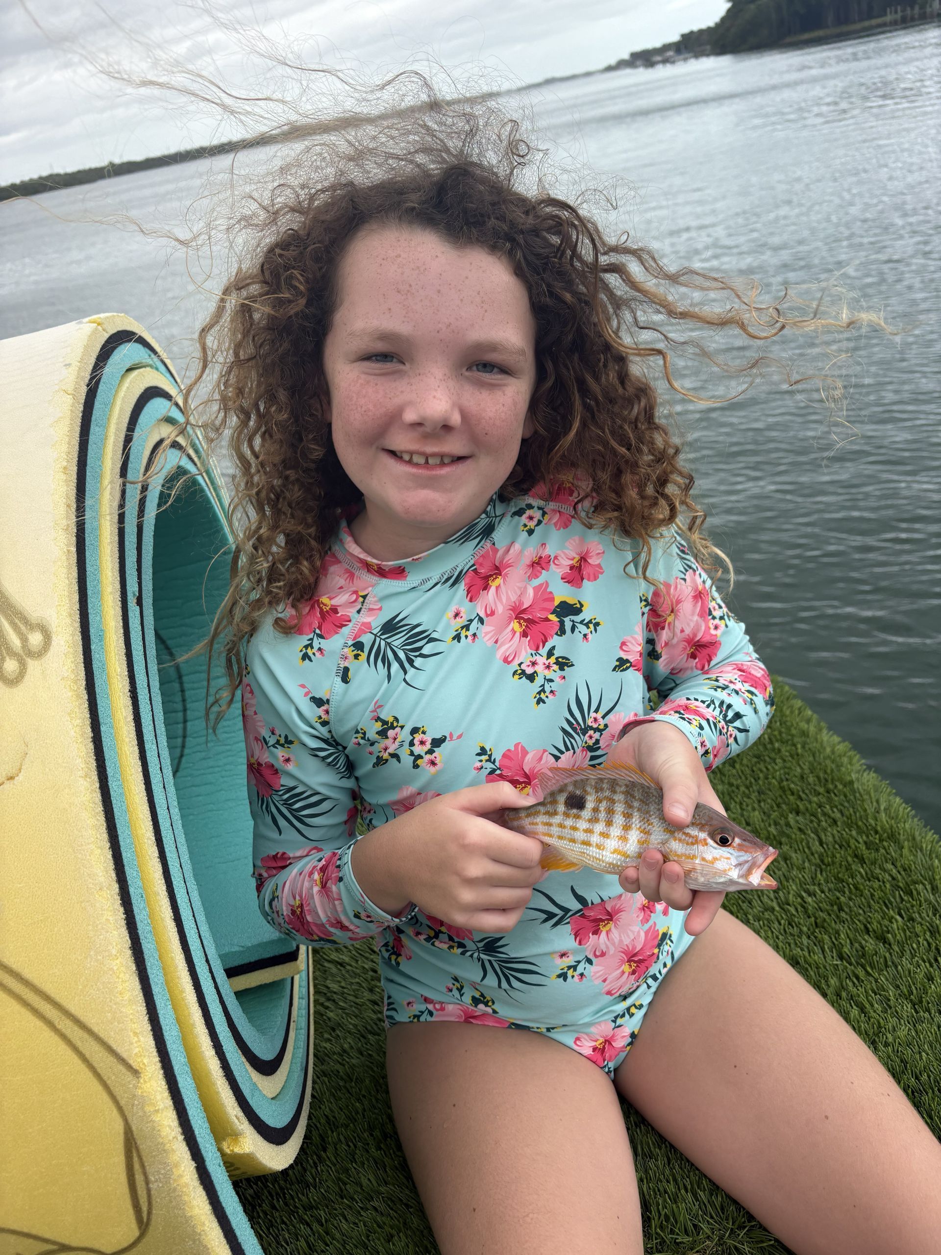 Child holding a fish beside a docked paddleboard on the water