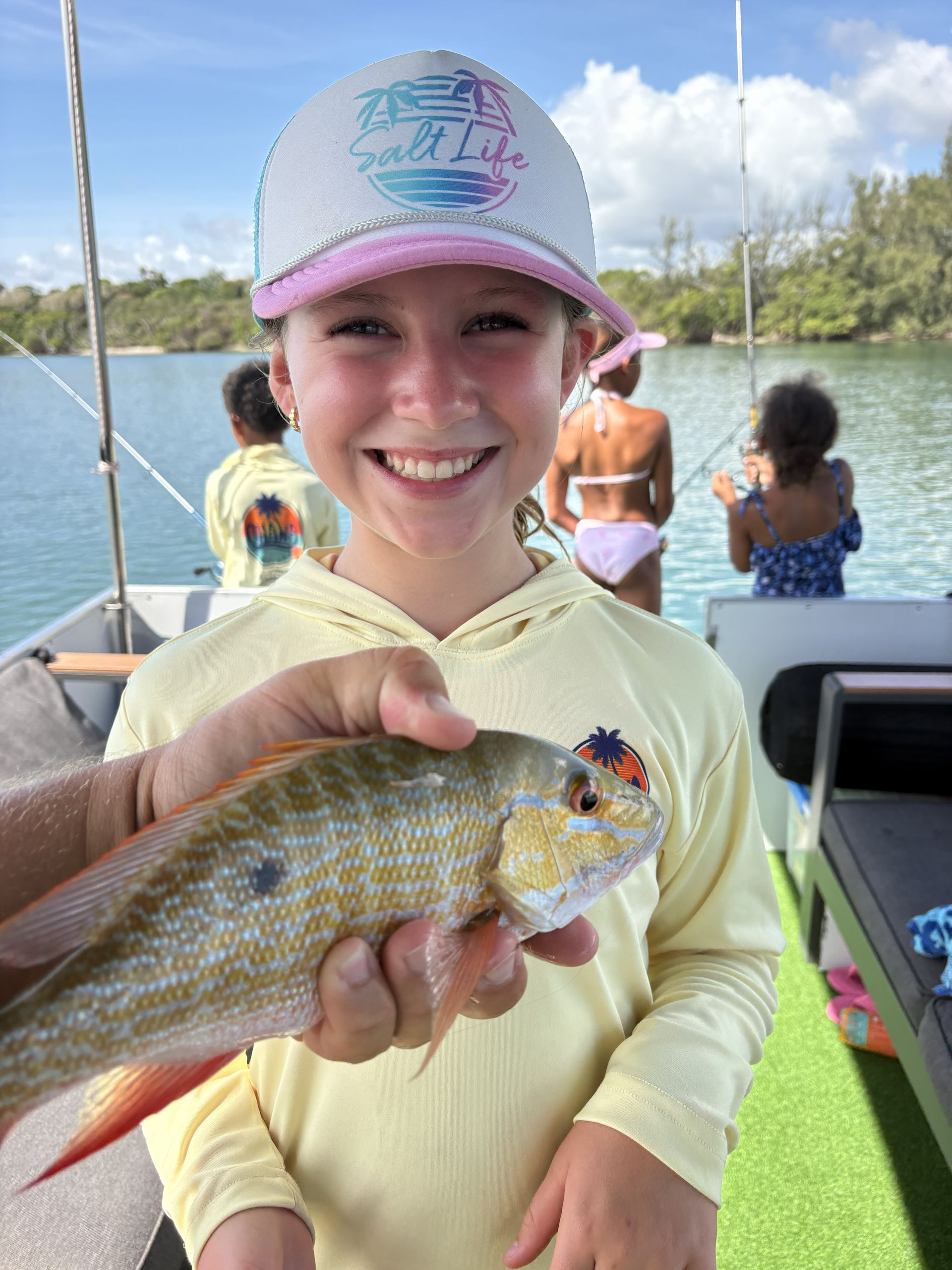 Smiling child holding a fish on a boat, with people and water in the background.