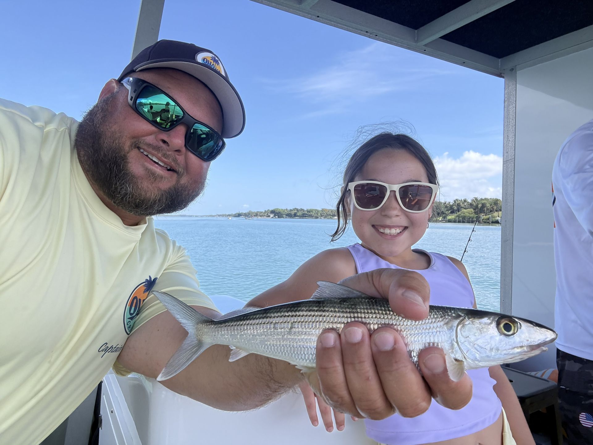 Two people on a boat smiling and holding a silver fish over blue water.