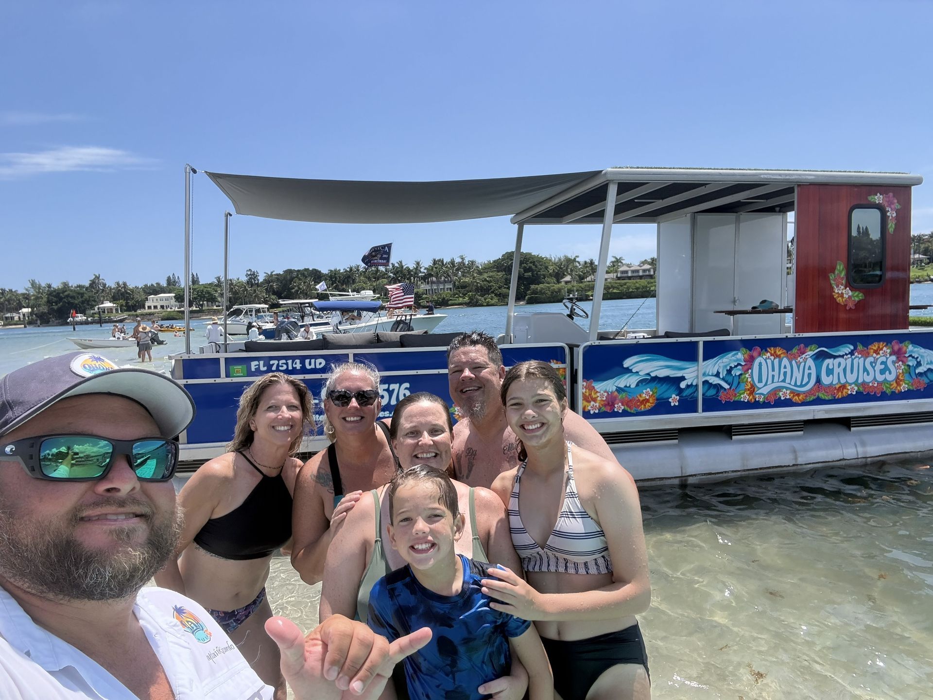 Group selfie on a boat with blue water, smiling at the camera near a dock under a sunny sky