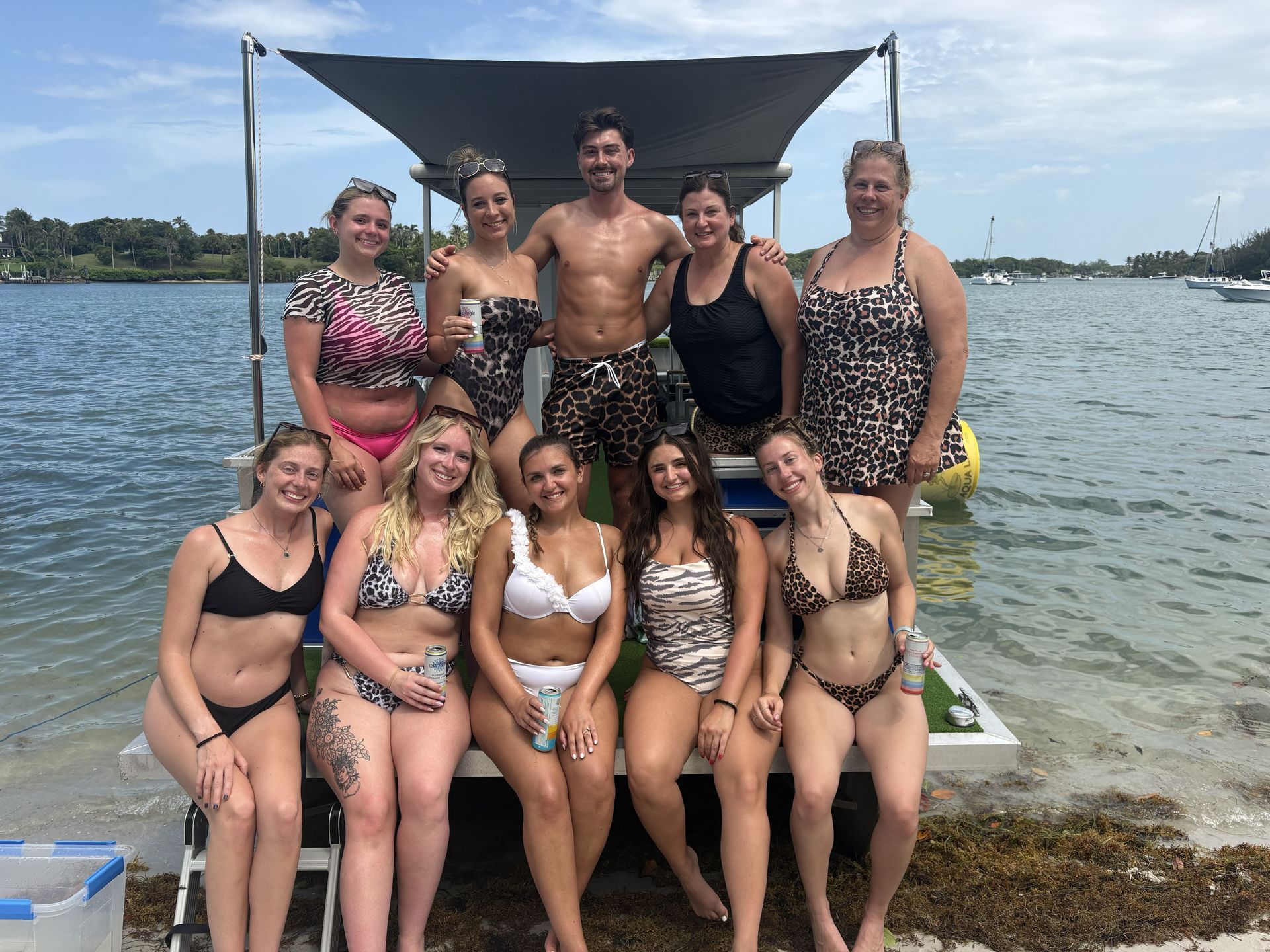 Group posing on a dock by the water, with a black canopy and a cloudy sky in the background.