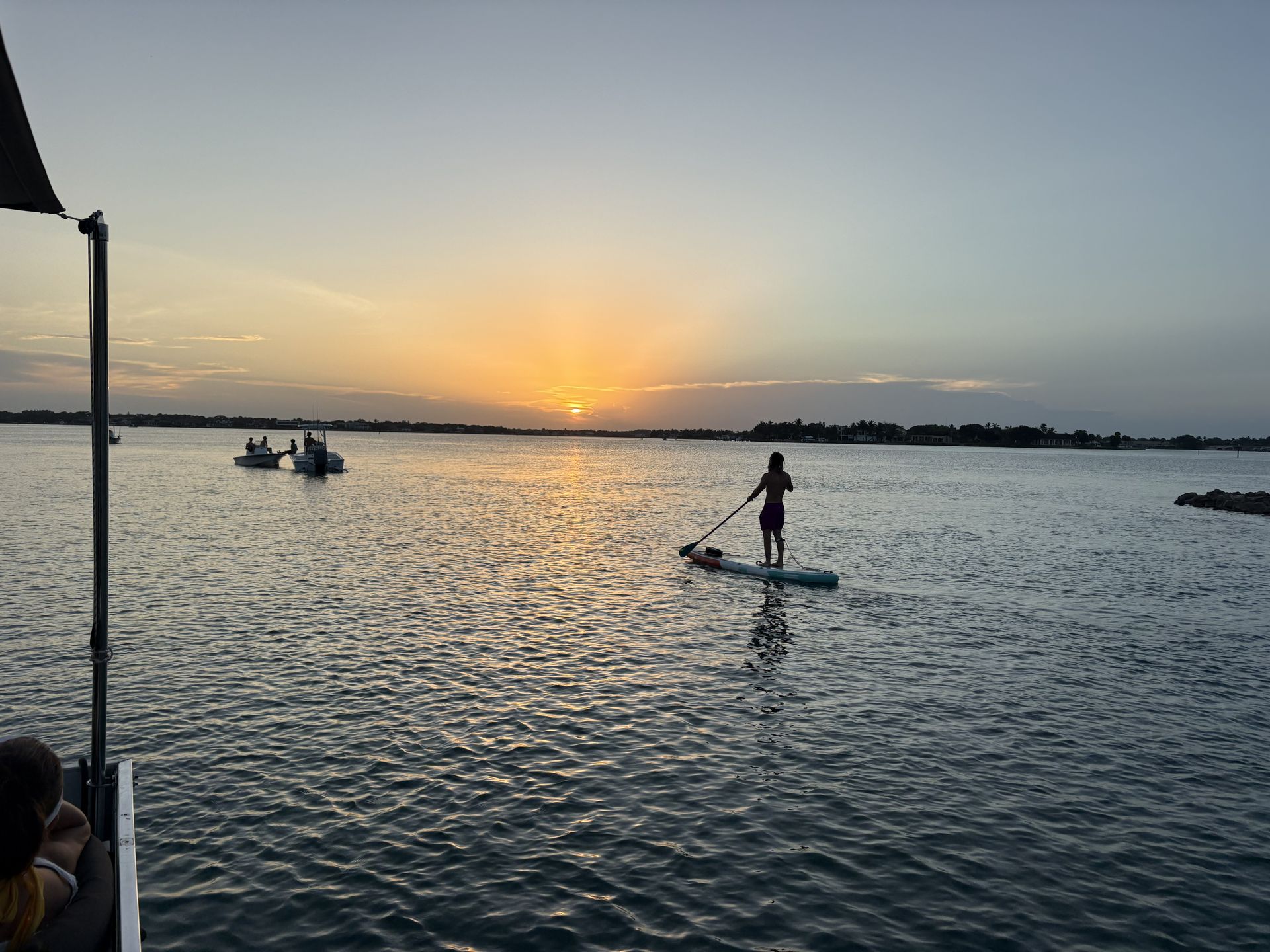 People paddle on calm water at sunset, with golden light on the horizon.