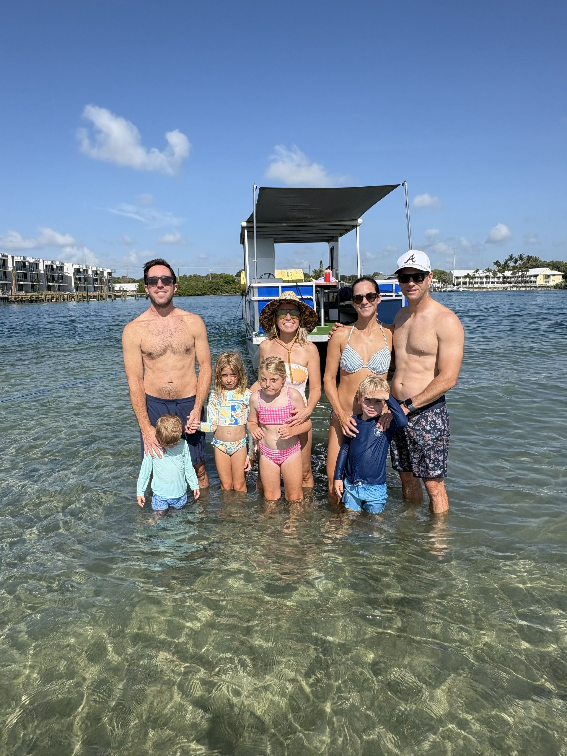 Family posing in shallow clear water near a dock on a sunny beach day
