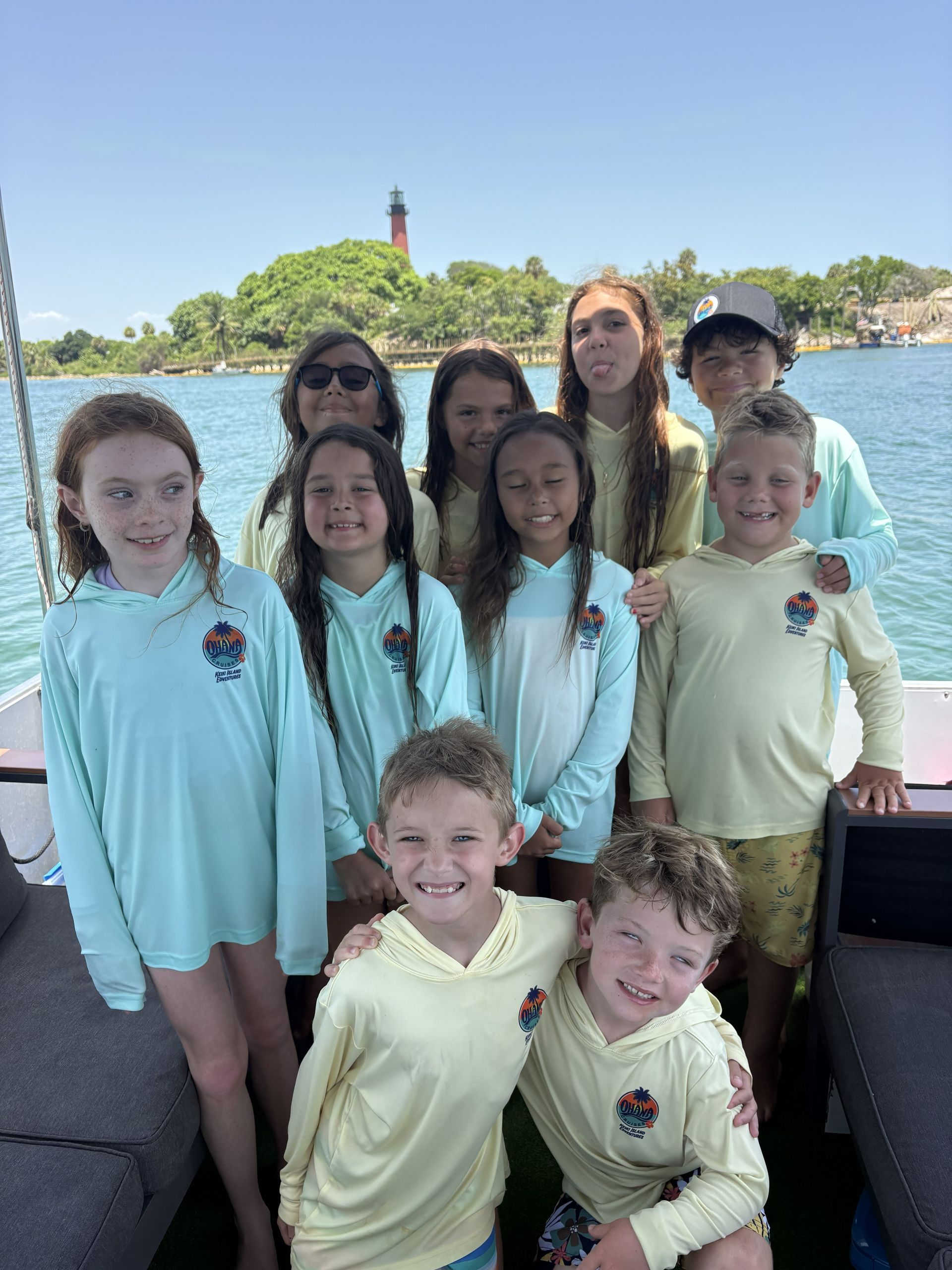 Group in light blue shirts posing by the water with a lighthouse in the background