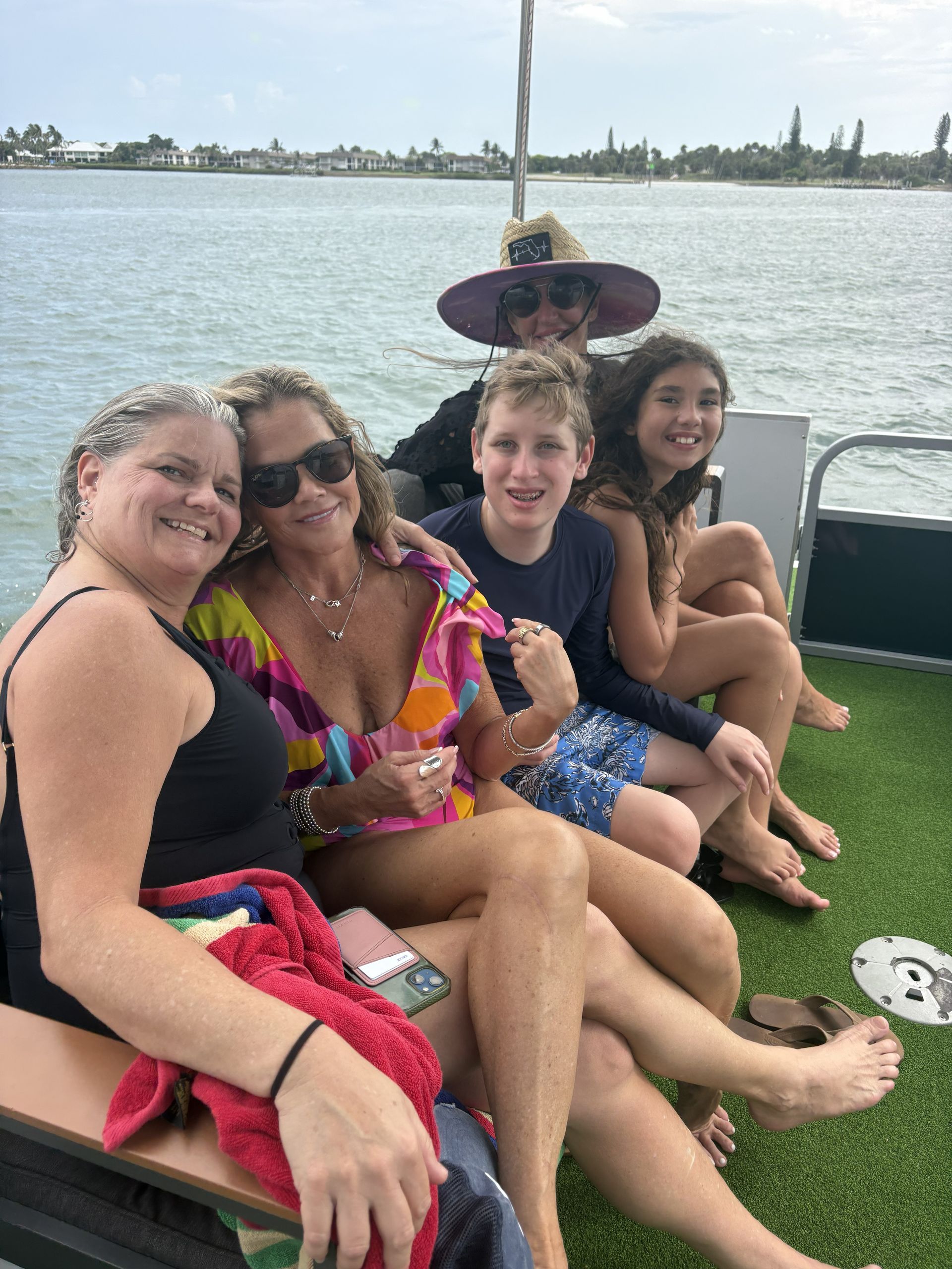 Four people sitting on grass by the water, smiling and relaxing on a lakeside dock.