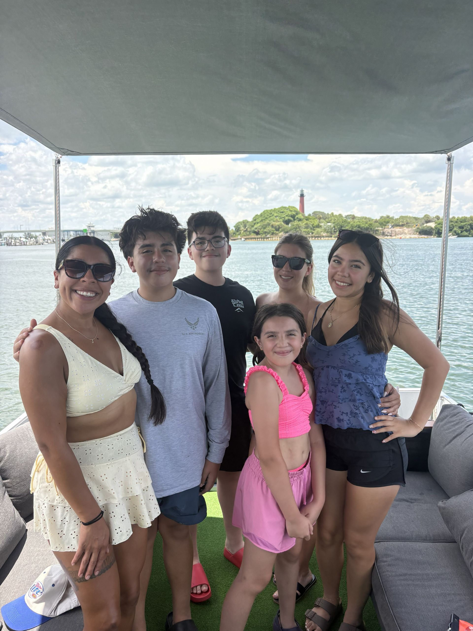 Five people posing on a boat under a canopy, smiling on the water with a shoreline in the background.