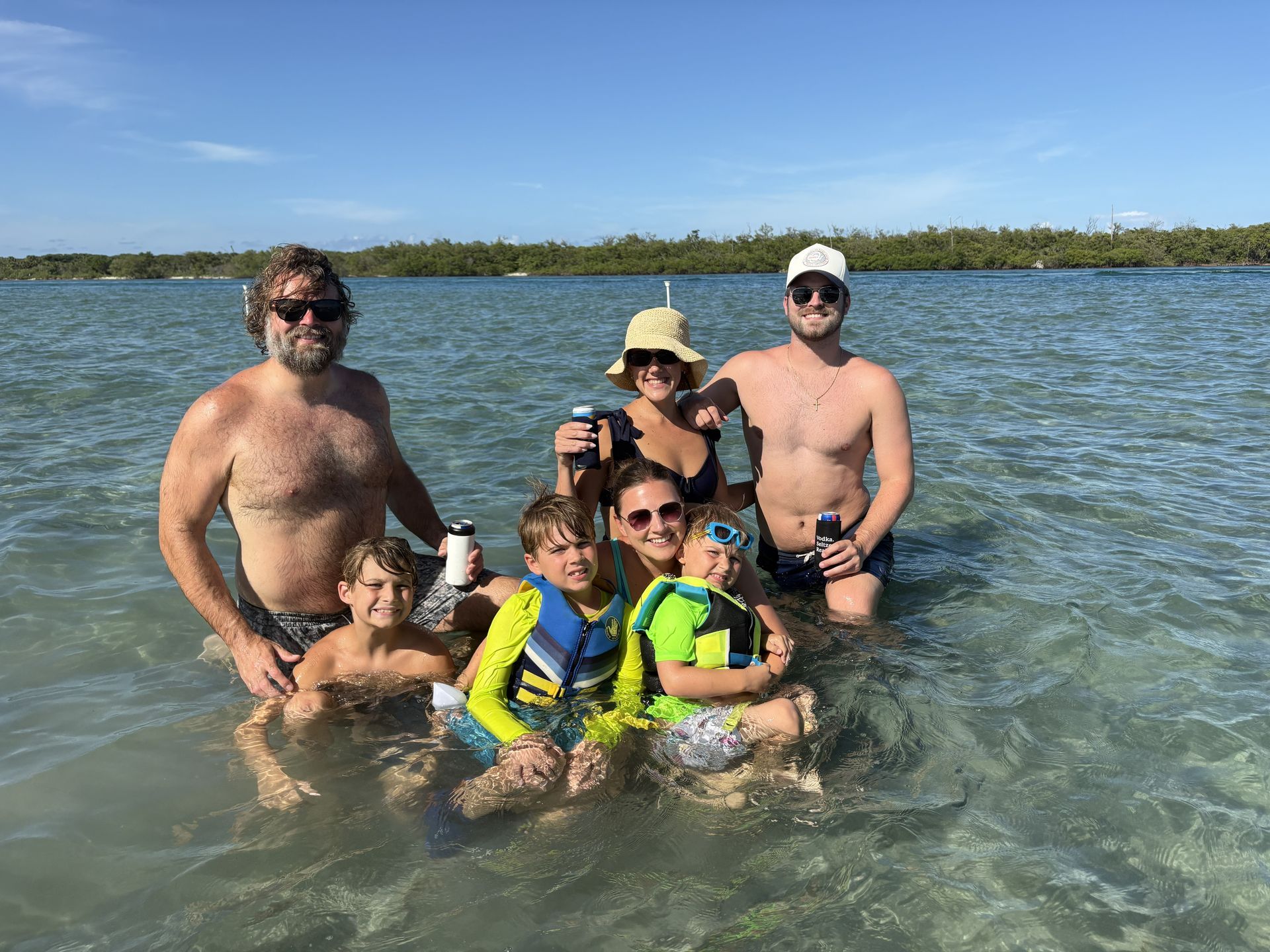 Group of people wading in shallow lake water on a sunny day, smiling and posing together