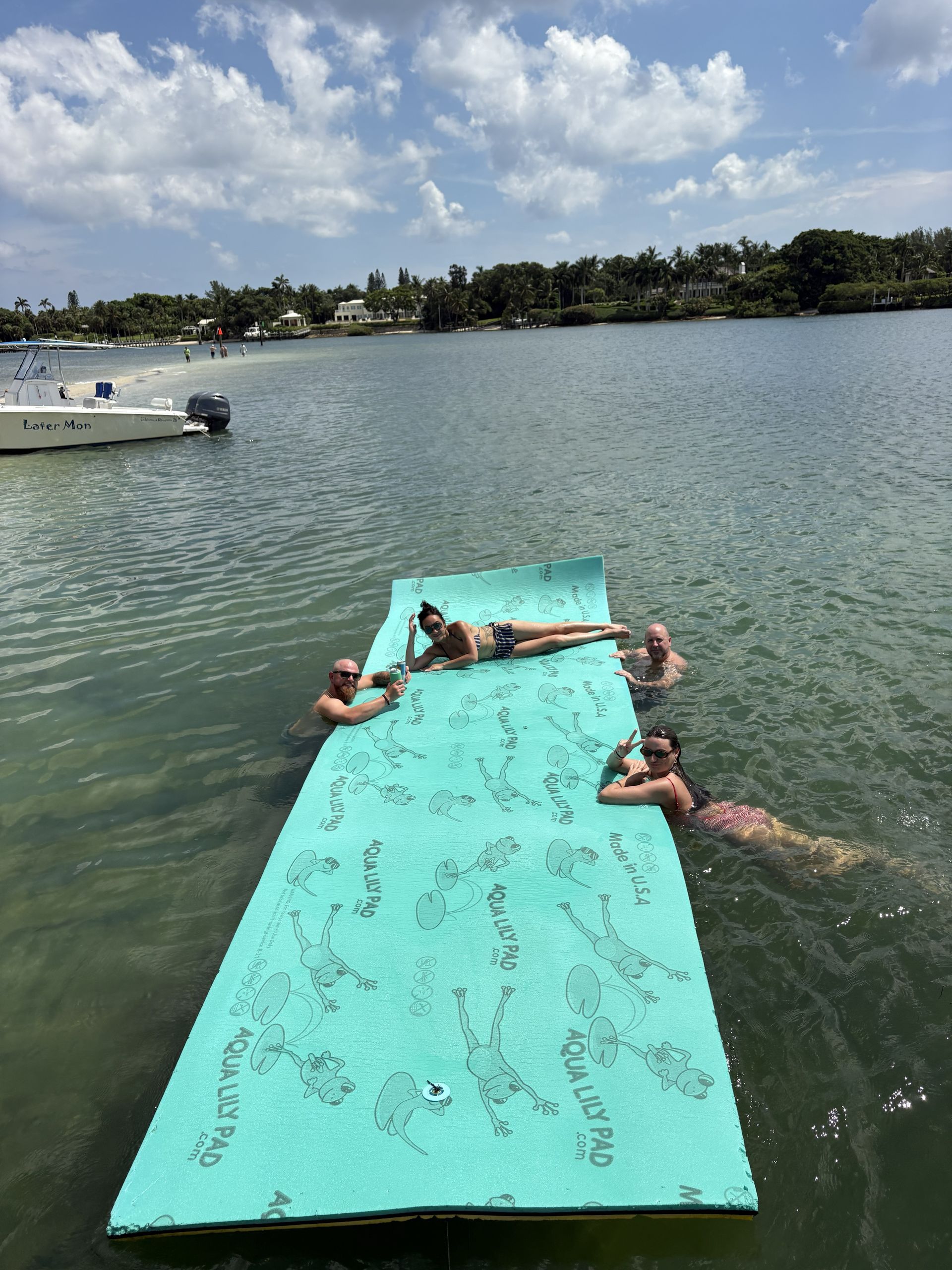 People floating on a turquoise mat in a lake on a sunny day