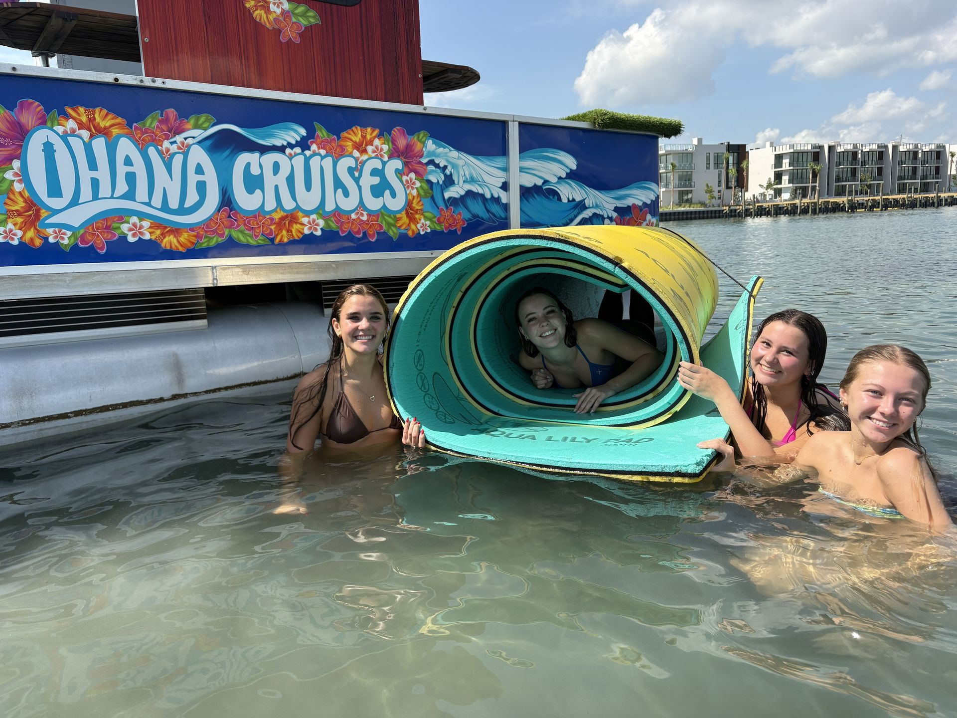 People in a water slide tunnel at Ohana Cruises, smiling in shallow water near a boat.