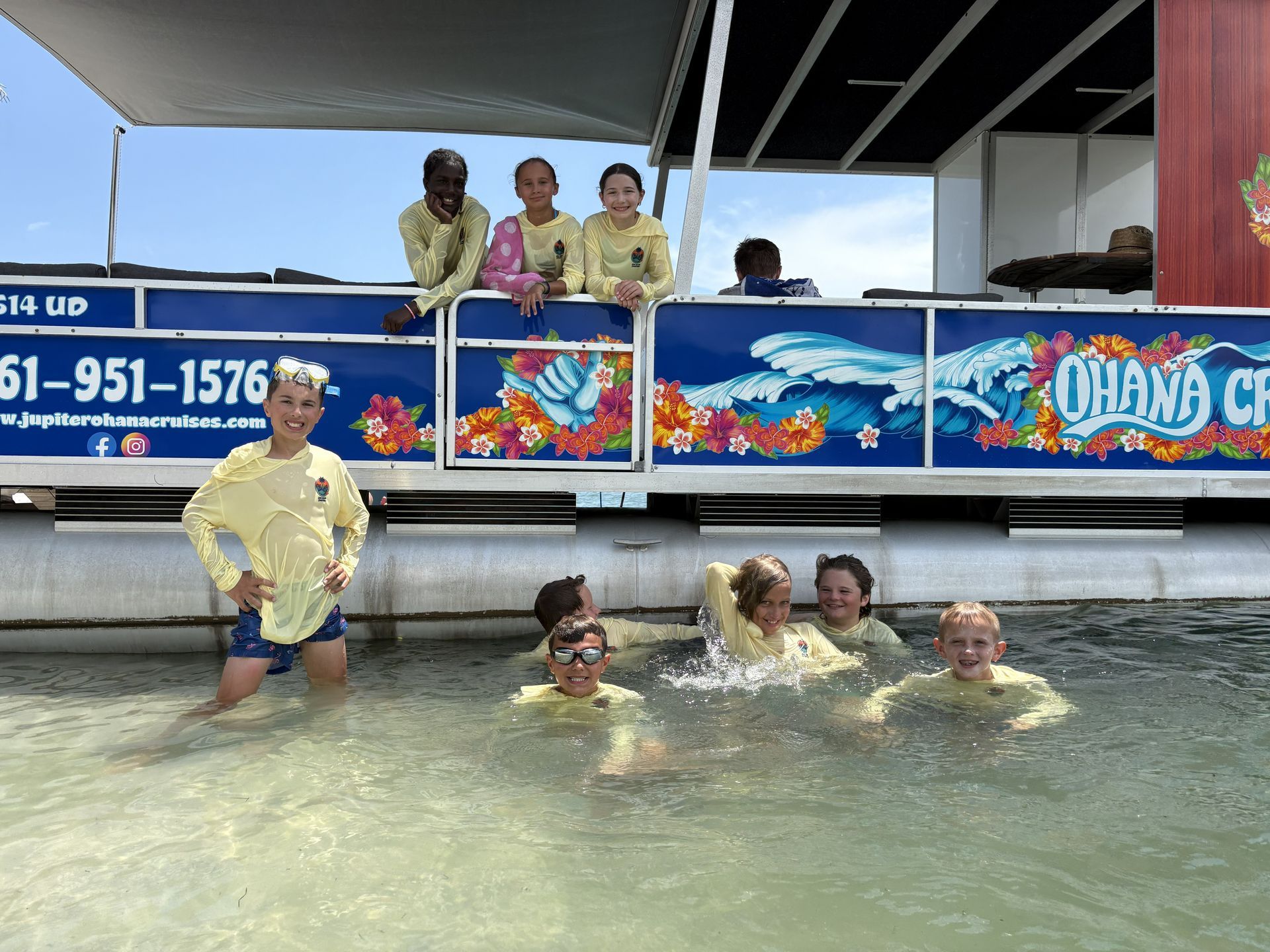 People in a pool at a boat dock, splashing in shallow water near a colorful mural.