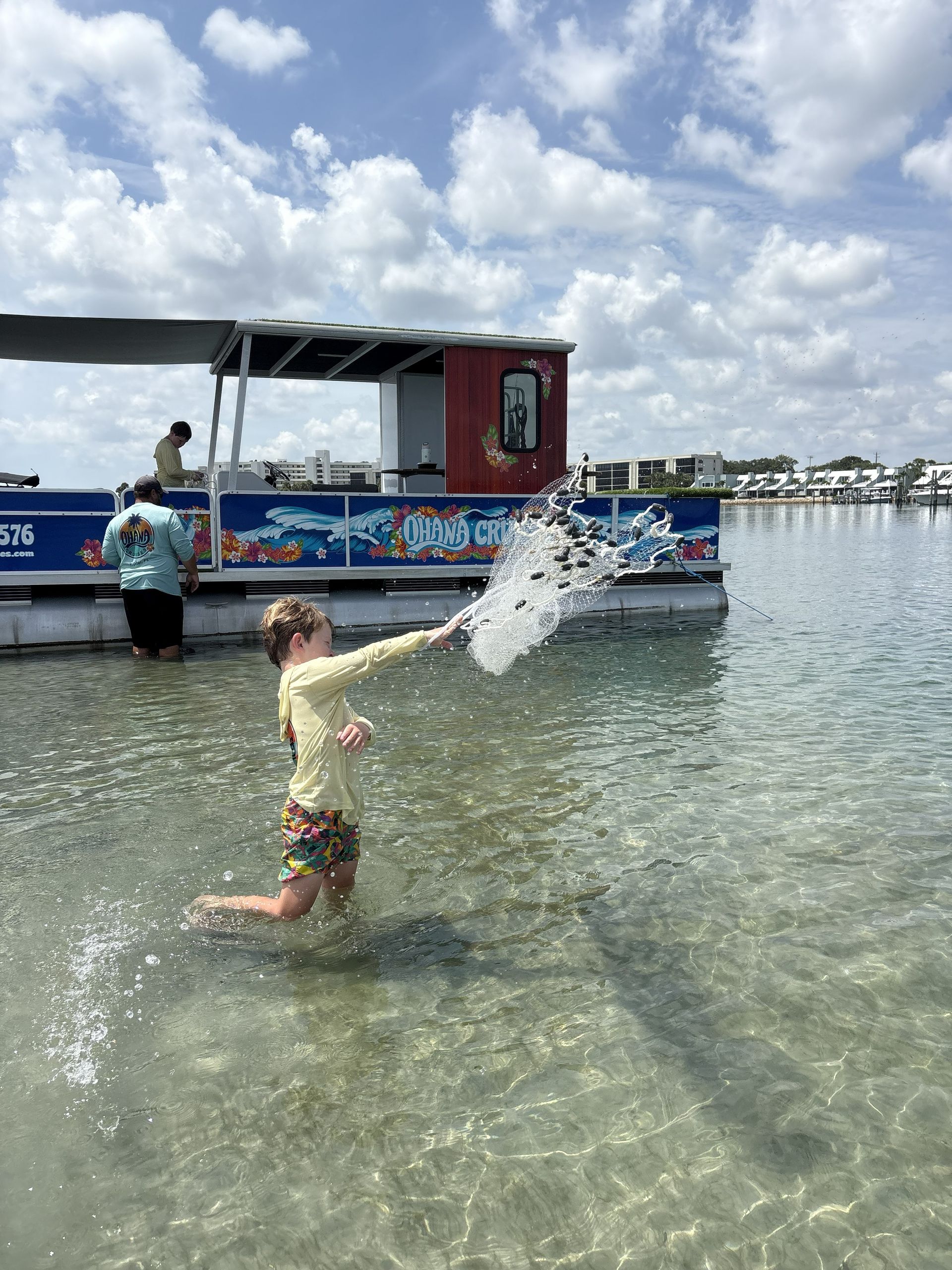 Child splashing in shallow water beside a decorated boat under a cloudy sky