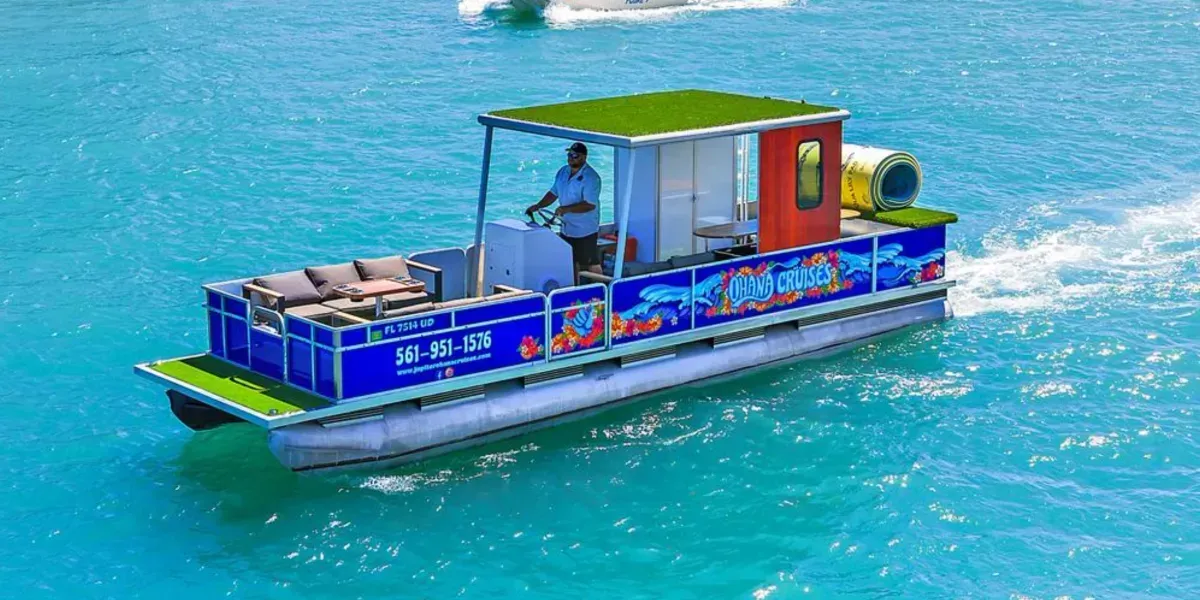 Small blue-and-red pontoon boat on turquoise water, carrying people and equipment under a green roof
