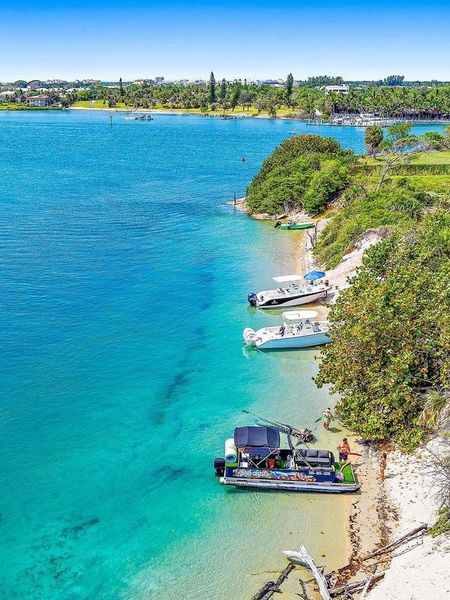 Turquoise bay with small boats docked along a rocky, tree-lined shore under a bright sky