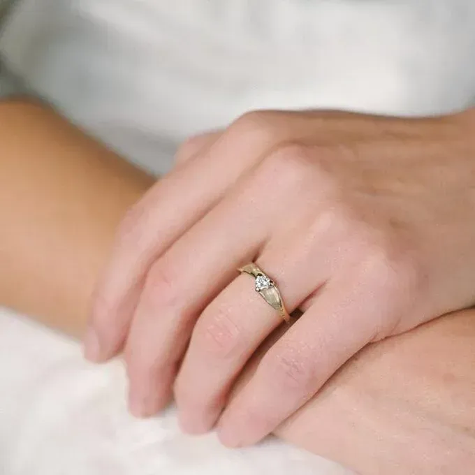 De hand van een persoon draagt een gouden ring met een kleine steen in het midden.