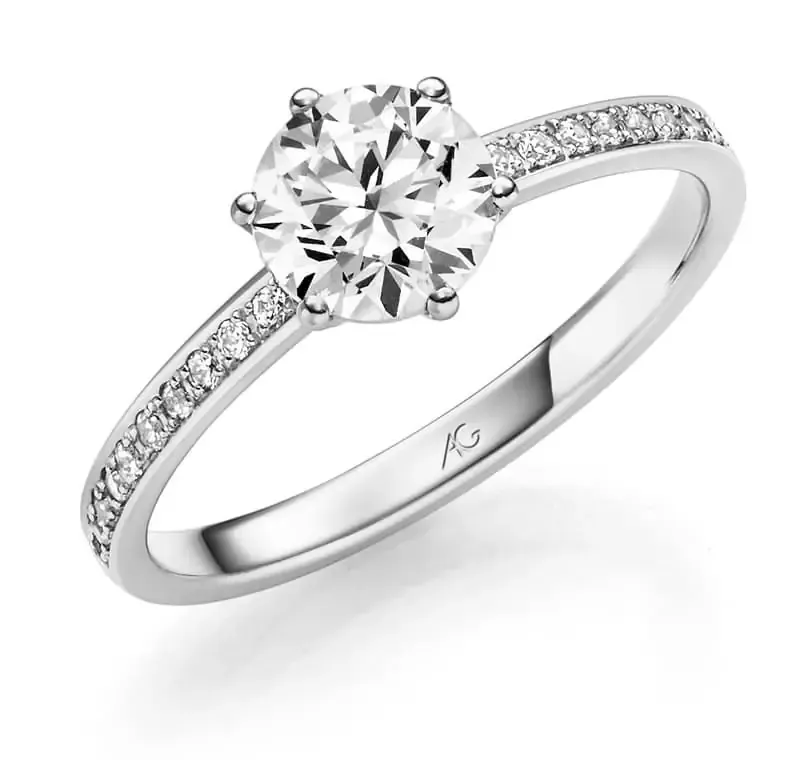 Verlovingsring met diamant, met een grote middelste steen en kleinere stenen langs de band, gezet in wit metaal.