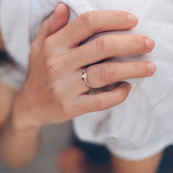 Close-up van een hand met een delicate ring aan de ringvinger, rustend op witte stof.