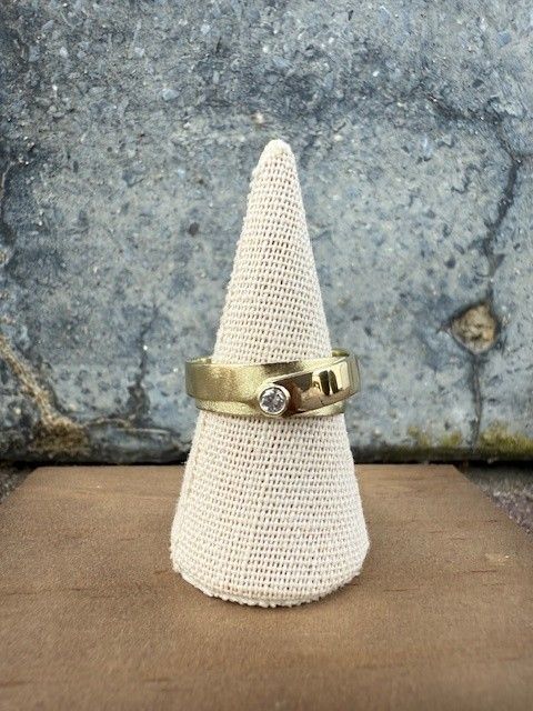 Gouden ring met een klein diamantje op een crèmekleurige kegel voor een grijze muur met textuur.