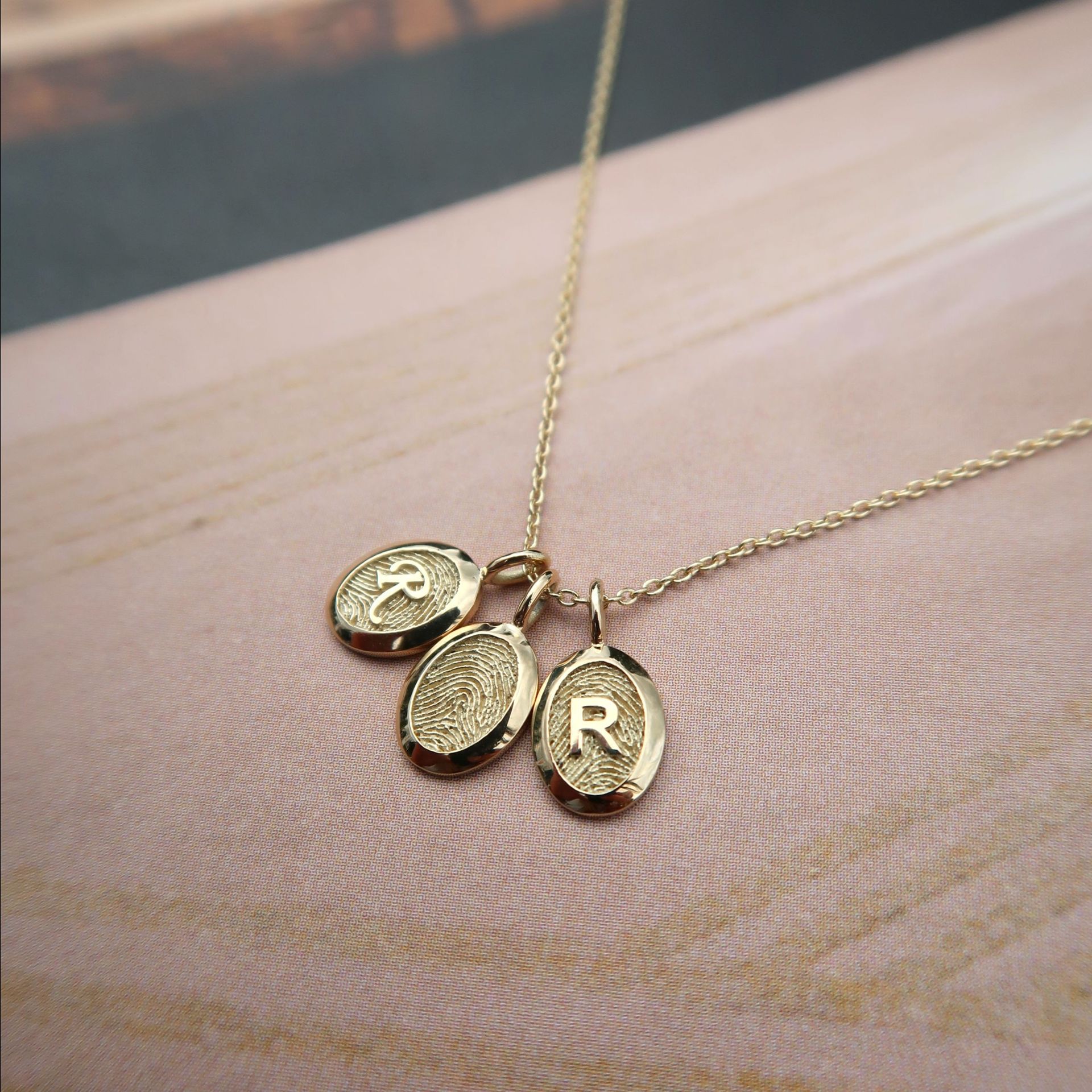 Gouden ketting met drie ovale hangers, waarvan één met de letter 