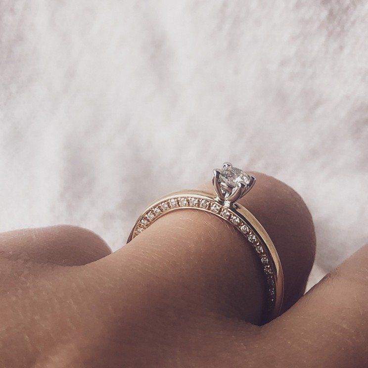 Verlovingsring met diamant aan de vinger, gouden band met kleinere diamanten.