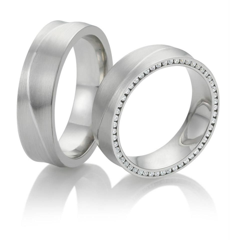 Twee zilveren trouwringen, één met een golvend ontwerp en de ander met een rij kleine edelstenen.