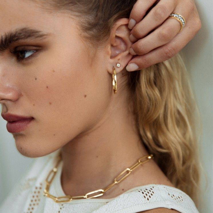 Vrouw draagt gouden oorringen, steker, ketting en ring; close-up.