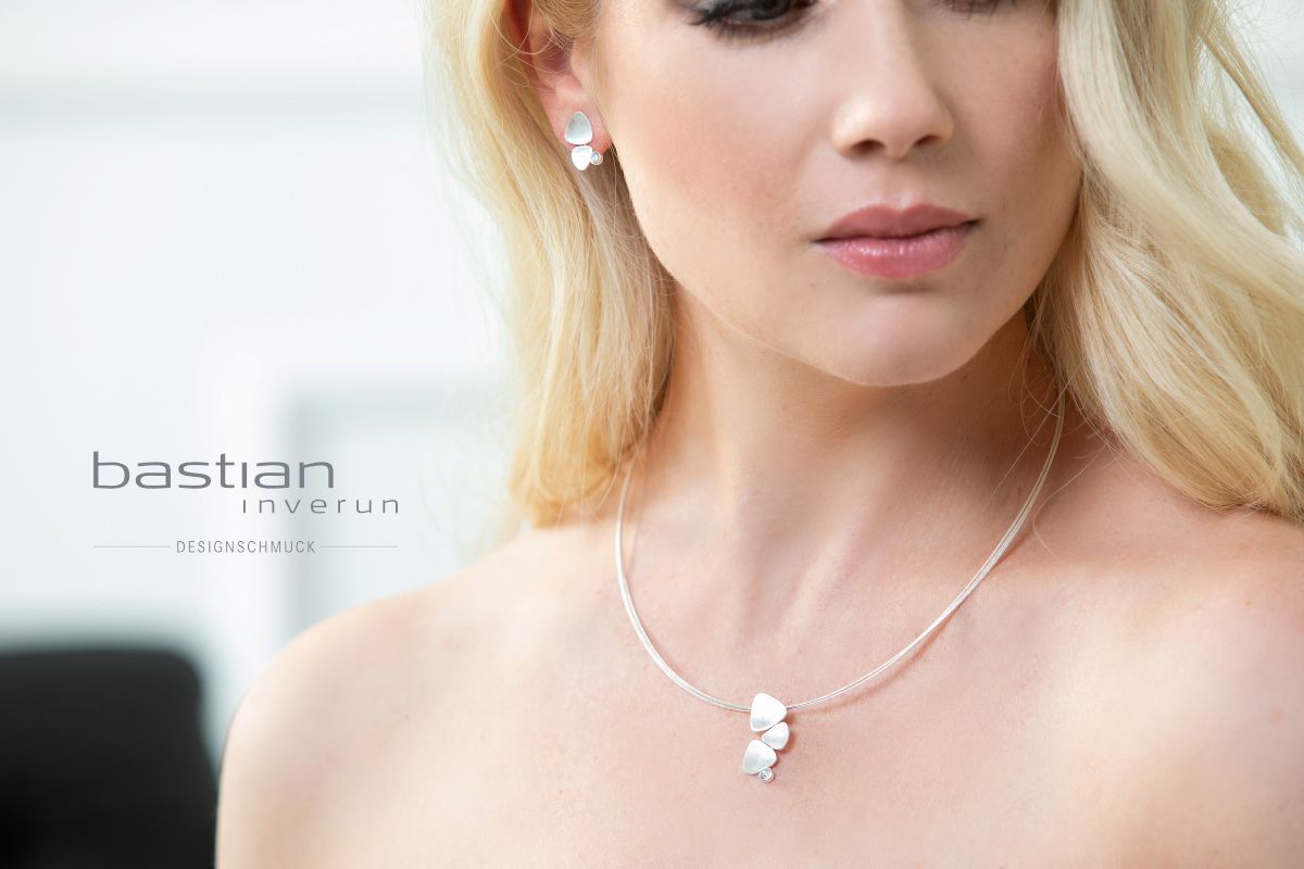 Vrouw draagt zilveren ketting en oorbellen; sieraden van het merk Bastian.