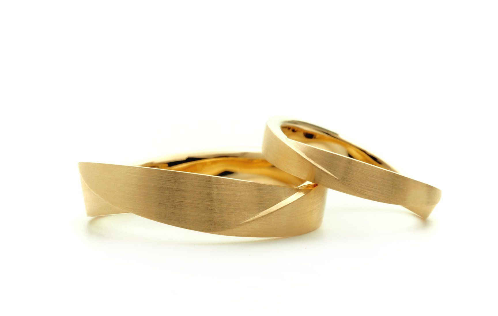 Twee gouden trouwringen met een structuurafwerking, liggend op een witte ondergrond.