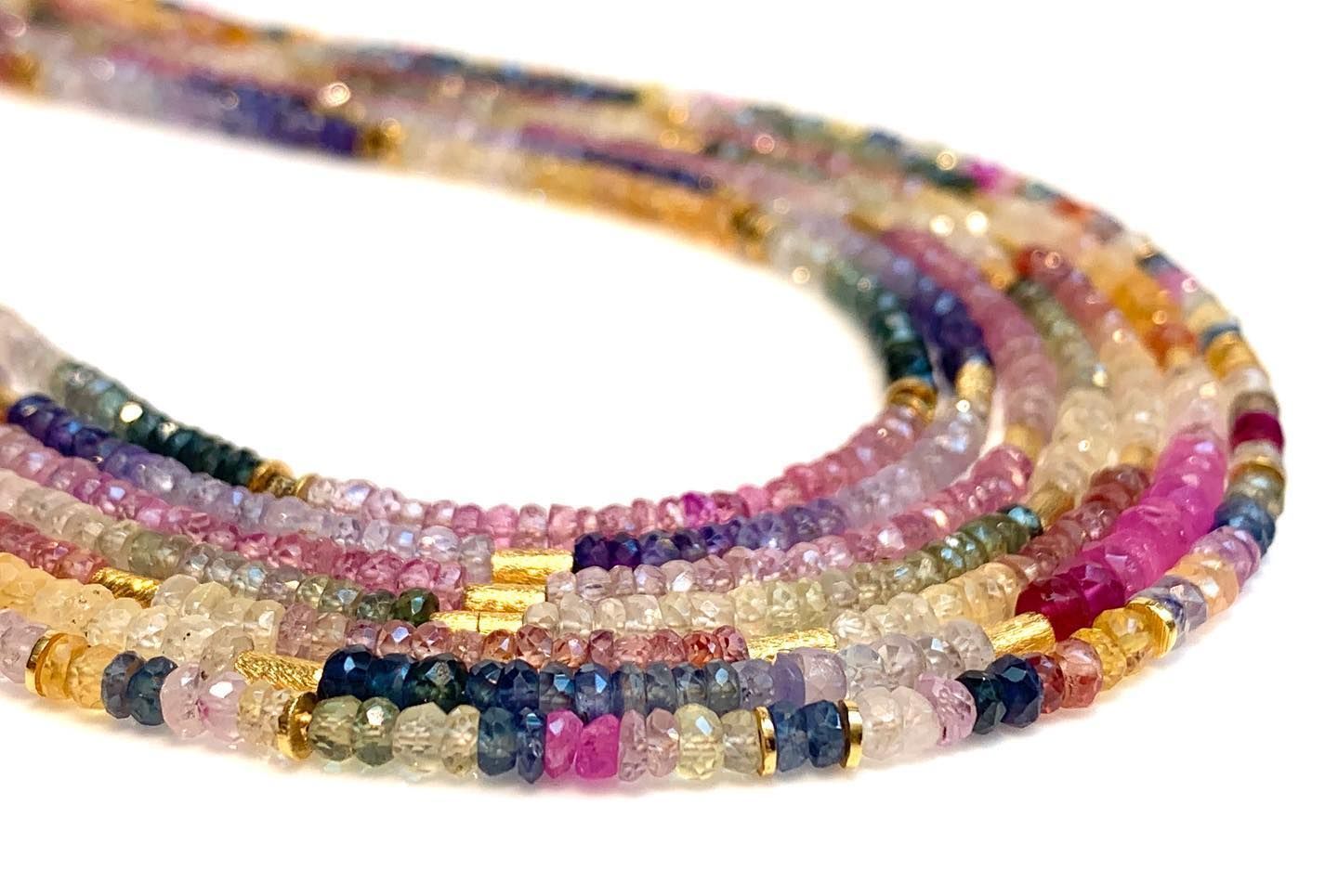 Slierten kleurrijke saffierkralen, verschillende tinten roze, blauw en geel, met gouden accenten.