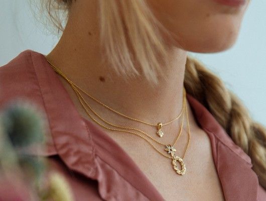 Vrouw draagt meerdere gouden kettingen, roze topje en blonde vlecht.