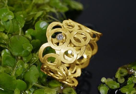 Gouden ring met diamantaccent, gezet tussen groene waterplanten.