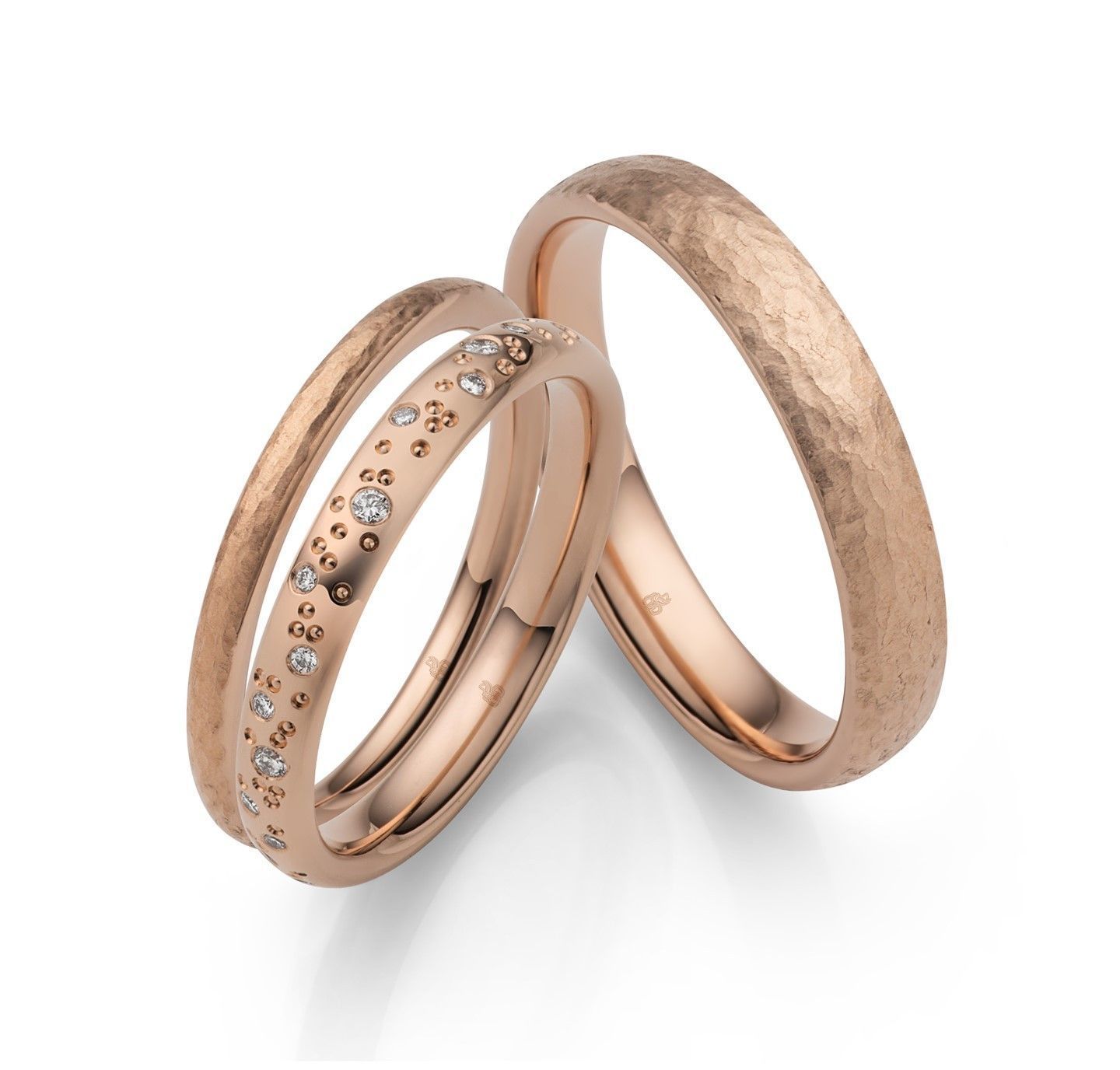 Twee trouwringen van roségoud, één met diamanten en de andere met structuur.