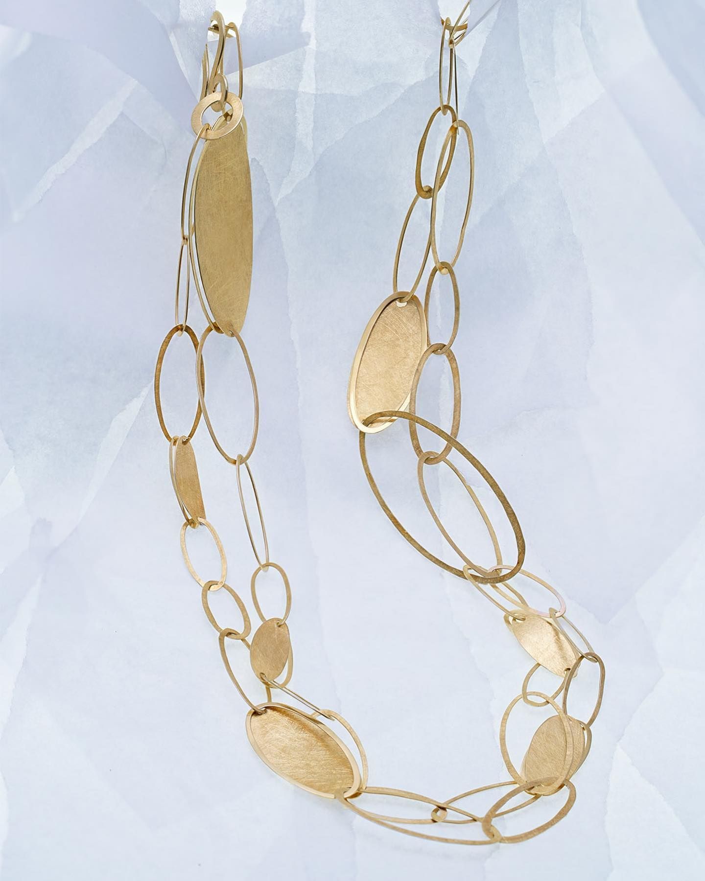 Gouden ketting met ovale en langwerpige schakels, hangend tegen een lichte achtergrond.