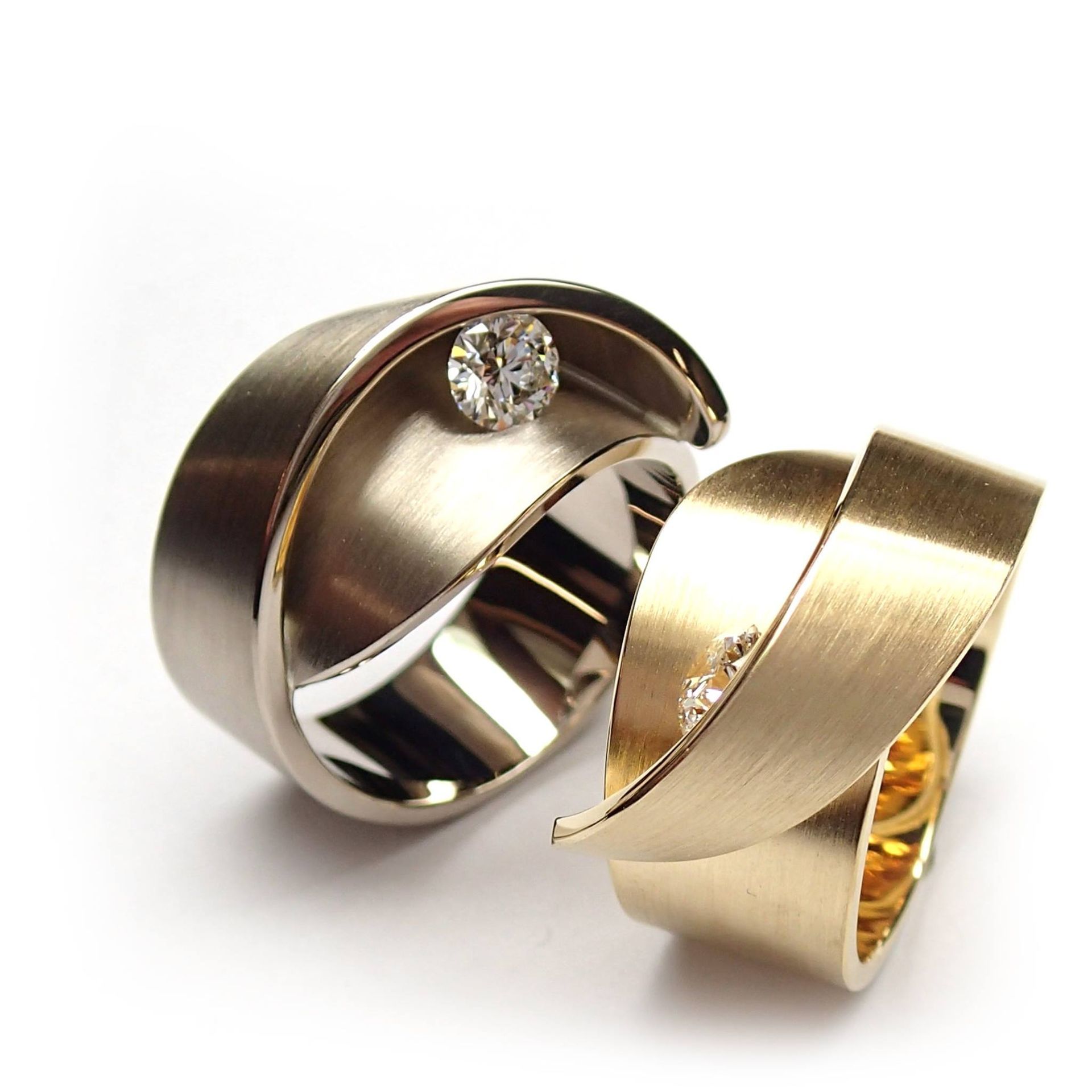 Twee gouden ringen met gebogen, geborsteld metalen design, waarvan één met een diamant.