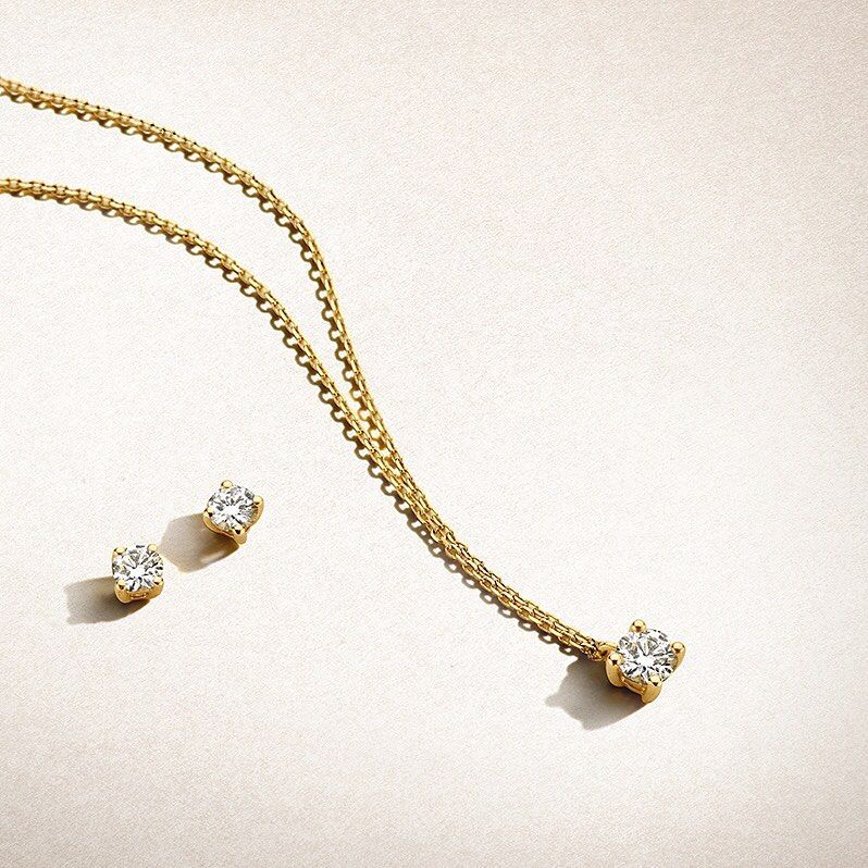 Gouden diamanten ketting en bijpassende oorbellen op een crèmekleurige achtergrond.