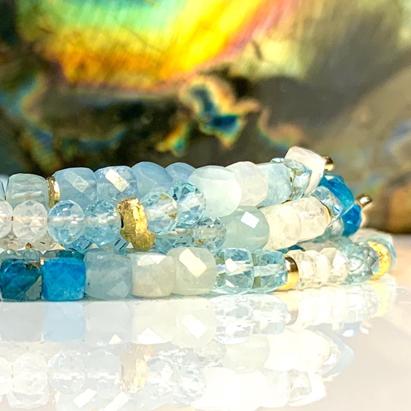 Stapel blauwe en witte kralenarmbanden met gouden accenten, die het licht reflecteren.