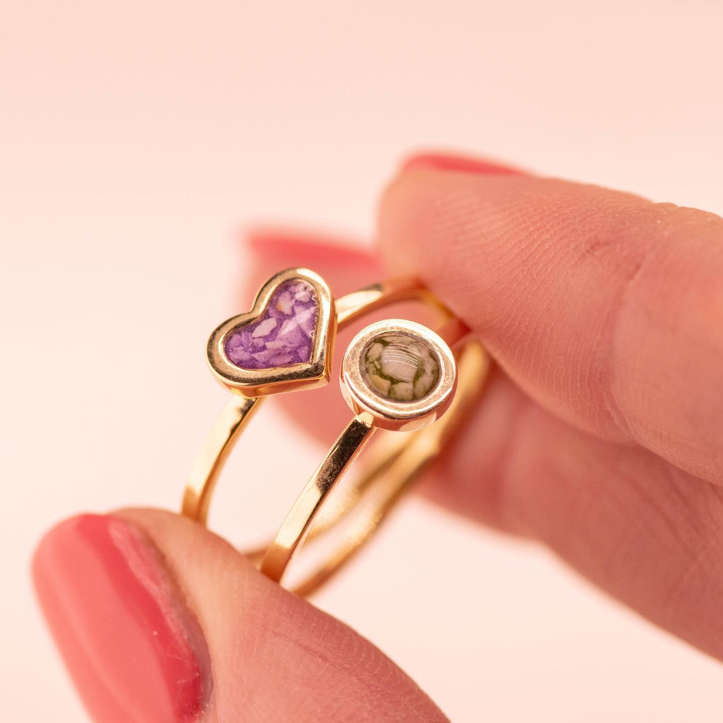 Twee gouden ringen, één hartvormig en paars, de andere rond en groen, vastgehouden door een persoon met gelakte nagels.