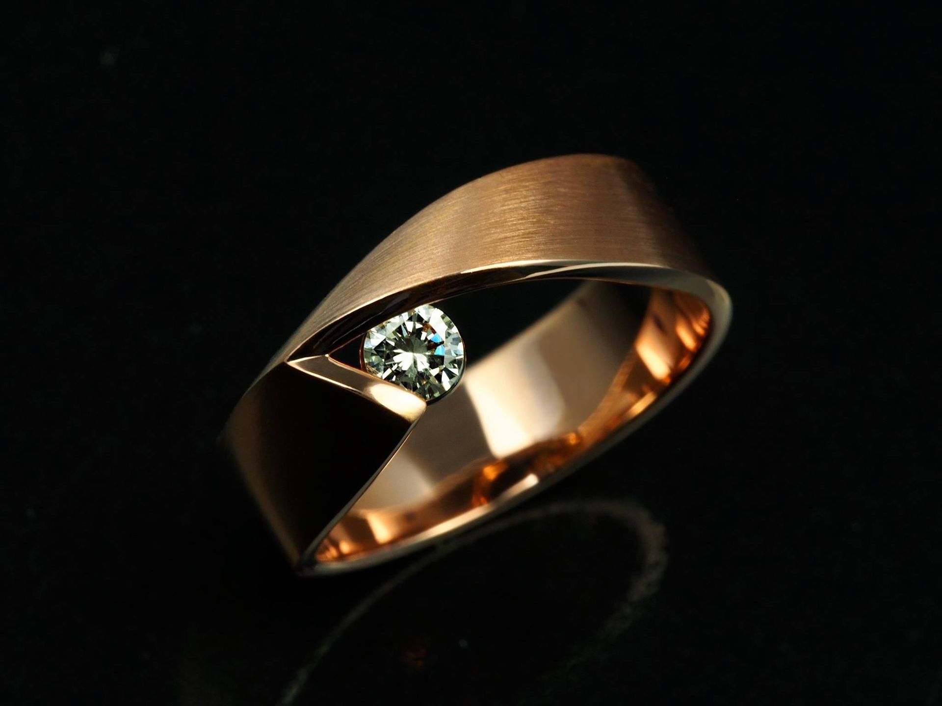 Roségouden ring met een diamant in het midden van een gebogen ontwerp op een zwarte achtergrond.