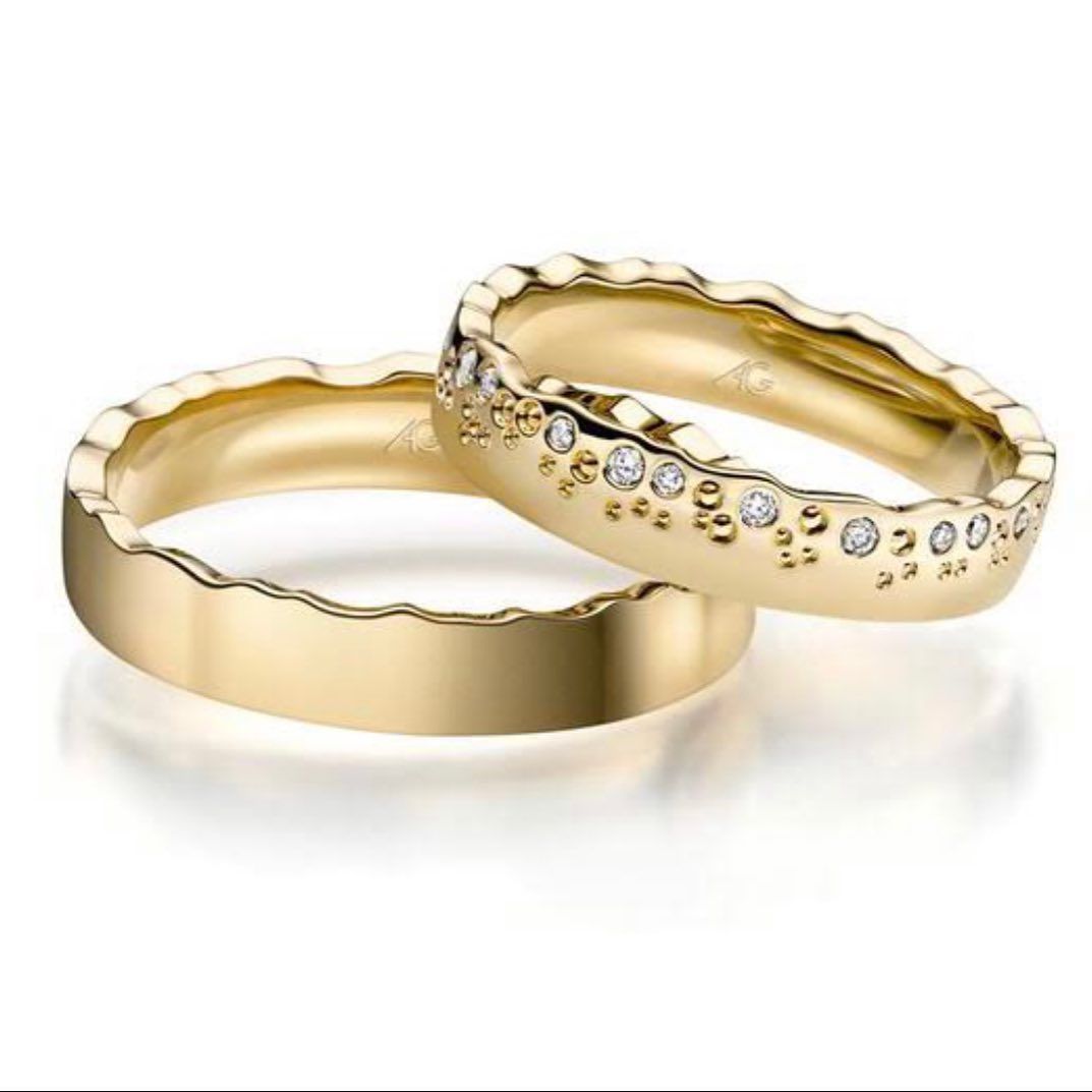 Twee gouden trouwringen, waarvan één met diamanten, op een witte achtergrond.
