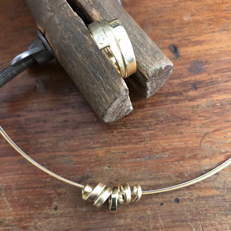 Close-up van gouden ringen en een ketting op een houten oppervlak, één ring vastgehouden in een klem.