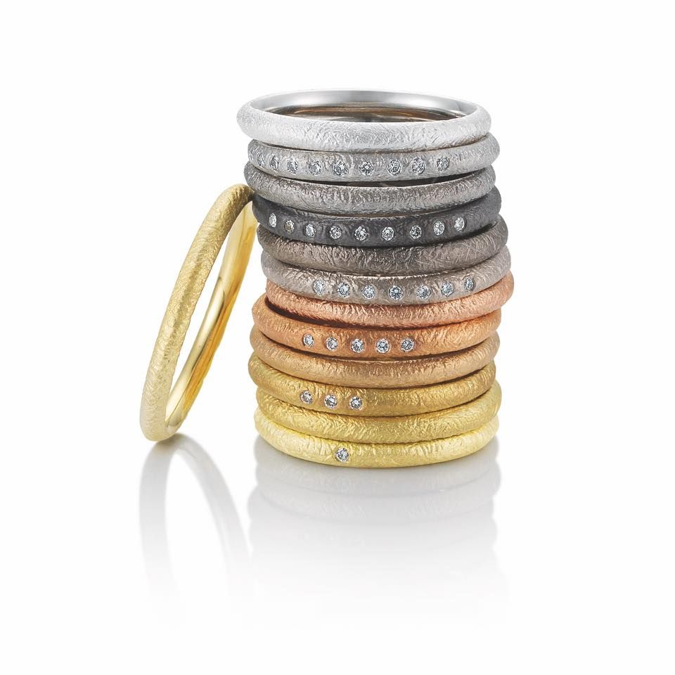 Stapel metalen ringen met textuur in verschillende kleuren, sommige met diamanten. Eén ring hangt aan de zijkant.