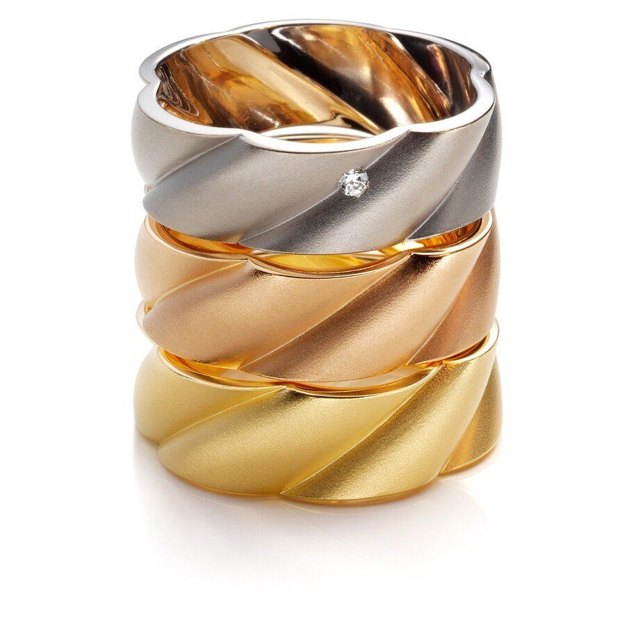 Drie gouden ringen in verschillende kleuren op elkaar gestapeld. Bovenste ring: zilver met een kleine diamant.