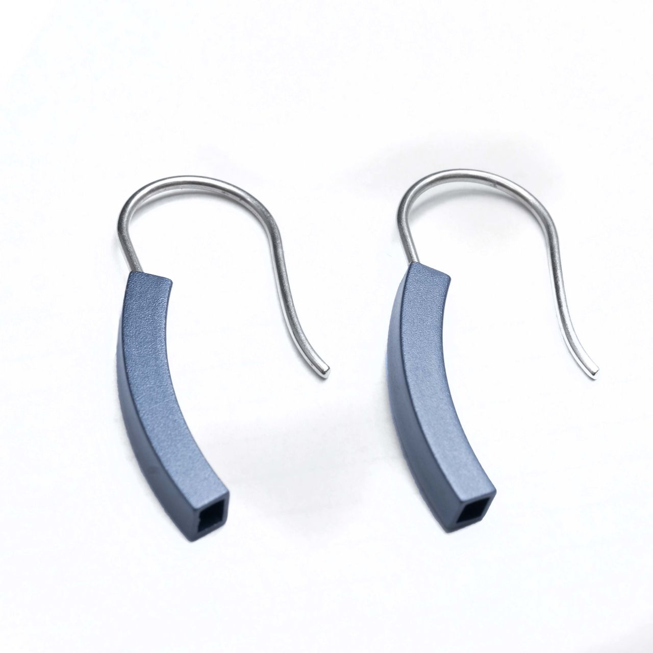 Twee minimalistische blauwe gebogen oorbellen met zilveren oorhaakjes.